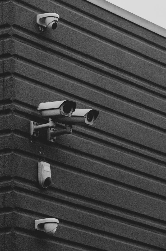 A black and white photo featuring multiple security cameras on a modern building wall.
